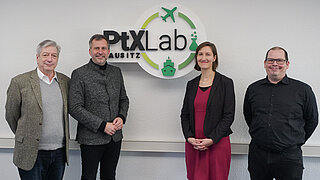 Cottbuser Oberbürgermeister Tobias Schick, neben dem Leitungsteam des PtX Lab Lausitz vor dem Logo des Kompetenzzentrums