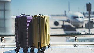 Koffer in der Abflughalle eines Flughafens, Flugzeug im Hintergrund, Sommerurlaub-Motiv, Koffer von Reisenden im Wartebereich eines Flughafenterminals, leere Halle mit großen Fenstern, Fokus auf die Koffer