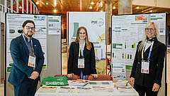 Three people standing around a presentation table in an exhibition hall.