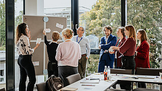 Eine Gruppe von Personen in Business-Kleidung vor einer Stecktafel in einem Konferenzraum.