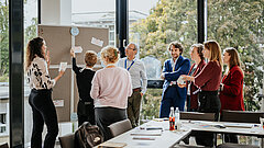 Eine Gruppe von Personen in Business-Kleidung vor einer Stecktafel in einem Konferenzraum.