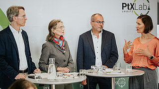 Vier Personen diskutieren auf einem Podium, eine spricht gestikulierend, die anderen hören aufmerksam zu.