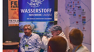 Abbildung von einer Gruppe von Vortragenden, von denen einer zu den Teilnehmenden spricht