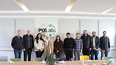 A group of women and men stand side by side in a row. Behind them on the wall is the PtX Lab Lausitz logo.