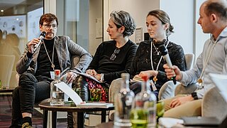 Four people are sitting at a table to take part in a panel discussion.