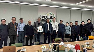 Eine vietnamesische Delegation und Vertreter des PtX Lab Lausitz stehen gemeinsam für ein Gruppenfoto in einem Besprechungsraum. Im Hintergrund ist das Logo des Labs an der Wand zu sehen, im Vordergrund ein Konferenztisch mit Bewirtung.
