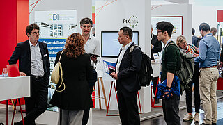 Mehrere Personen im Fachgespräch vor den Messeständen vom Cluster Dekarbonisierung der Industrie (CDI) und dem PtX Lab Lausitz auf der Hannover Messe.