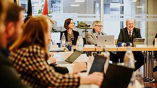 Männer und Frauen sitzen gut gelaunt in einem Konferenzraum am Tisch