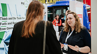 Anika Sieck vom PtX Lab Lausitz im fachlichen Gespräch mit einer Besucherin am Messestand auf der Hannover Messe 2025. Sie gestikuliert erklärend, während im Hintergrund die Infotafel des „Think and Do Tank“ sowie das Logo des Labs zu sehen sind.
