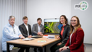 Three men and two women are sitting around a table and staring into the camera.