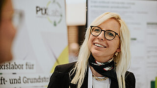 Zwei Personen, die miteinander sprechen. Im Hintergrund Stellwände mit Informationen.