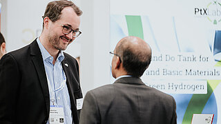 Sebastian Wiese-Beeg vom PtX Lab Lausitz im freundlichen Gespräch mit einem Besucher auf der Hannover Messe 2025. Er trägt ein Namensschild und lächelt; im Hintergrund ist ein Teil der Infotafel des „Think and Do Tank“ zu sehen.