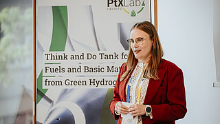 Eine Frau in Business-Kleidung steht vor einem Roll-Up des PtX Lab Lausitz.