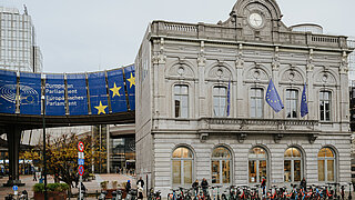A building on the right. There are people standing in front of it. On the left is a blue EU banner.