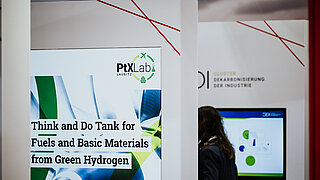 Nahaufnahme eines Messestands auf der Hannover Messe 2025. Im Vordergrund steht eine Infotafel des PtX Lab Lausitz mit der Aufschrift „Think and Do Tank for Fuels and Basic Materials from Green Hydrogen“. Im Hintergrund ist ein Panel des „Cluster Dekarbonisierung der Industrie“ (CDI) erkennbar.