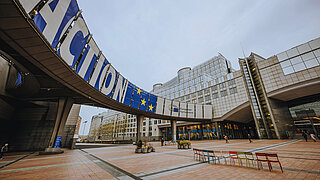Gebäude der Europäischen Union mit blauem Schriftzug "Action", daneben Logo des Europäischen Parlamentes.