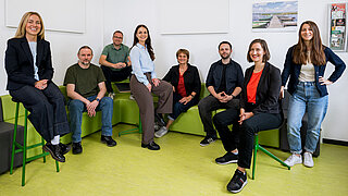 Eight people in a room with a green floor.
