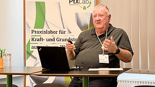 A person in the foreground. A banner and a whiteboard in the background.