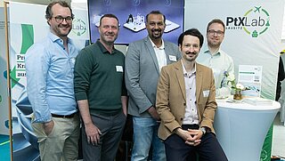 Group photo of five men at a trade fair stand.