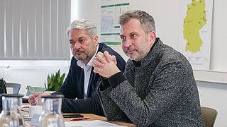 Oberbürgermeister Tobias Schick und Ralf Beyer, Referent für Wirtschaftsfragen der Stadt Cottbus, sitzen am Tisch und verfolgen des Gespräch