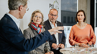Vier Diskutierende auf einem Panel sprechen engagiert über ein Fachthema. Im Hintergrund ist eine Leinwand mit Veranstaltungslogo sichtbar.