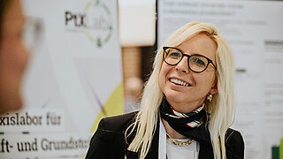 Zwei Personen, die miteinander sprechen. Im Hintergrund Stellwände mit Informationen.