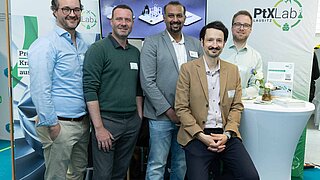 Fünf Mitarbeiter des PtX Lab Lausitz posieren vor ihrem Messestand