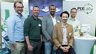 Five employees of PtX Lab Lausitz pose in front of their exhibition stand.