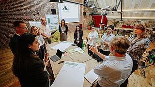 Several people are standing in a circle around a table in a room.