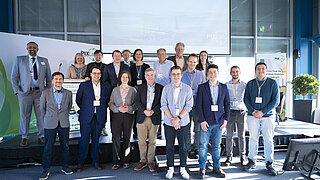 Eine Gruppe von Menschen steht auf einem Podium vor einer Pressewand.
