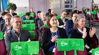 Mehrere Personen sitzen in einem Konferenzraum und klatschen.