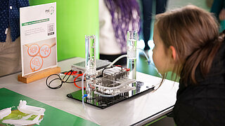 Ein junges Mädchen betrachtet einen Modell-Elektrolyseur.
