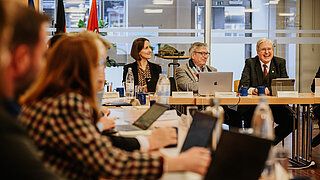 Several people are sitting at a conference table. A man is speaking to the participants.