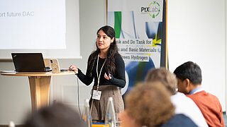 Frau an Stehtisch spricht zu Publikum. Dahinter Rollup des PtX Lab Lausitz.