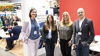 Vier Personen stehen an einem Messestand.