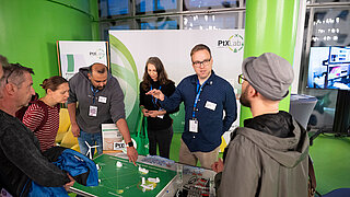 Experten des PtX Lab Lausitz erklären Besuchern an einem Messestand den Herstellungsprozess von nachhaltigen Kraftstoffen anhand eines Modells und einer Grafik.